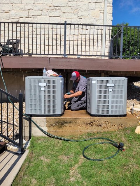 Holman Comfort Systems technician servicing a dual outdoor AC system on a Central Texas home