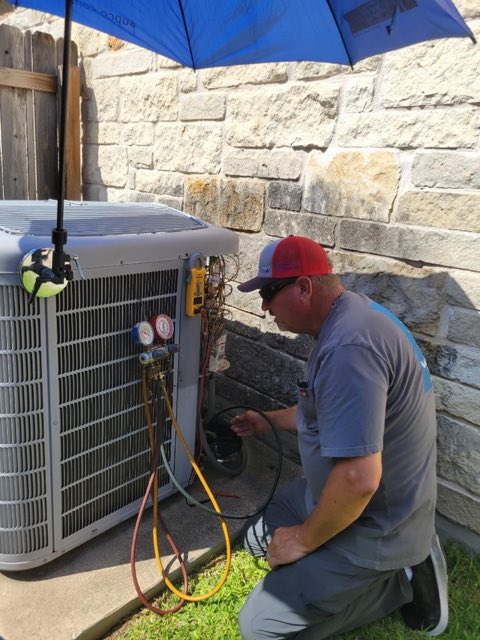 Holman Comfort Systems technician charging a residential AC condenser with refrigerant gauges in Round Rock, TX